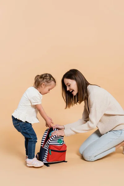 Girl with down syndrome and excited mother looking at backpack on beige — Stock Photo