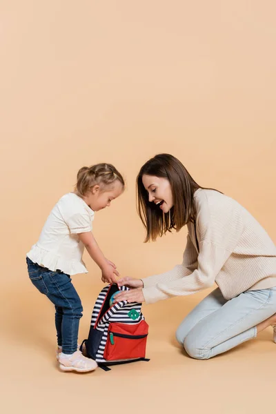 Girl with down syndrome and excited mother looking at backpack on beige — Photo de stock