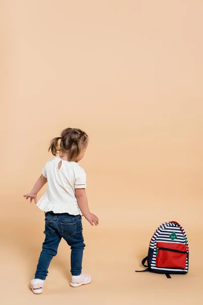 Kid with down syndrome walking near backpack on beige — Stockfoto
