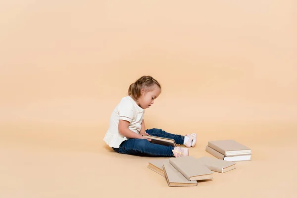 Дитина з синдромом Дауна, що сидить біля книг на бежевому — стокове фото