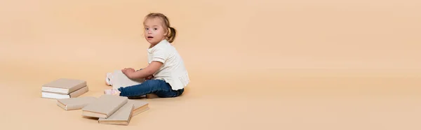 Girl with down syndrome sitting near books on beige, banner — Fotografia de Stock