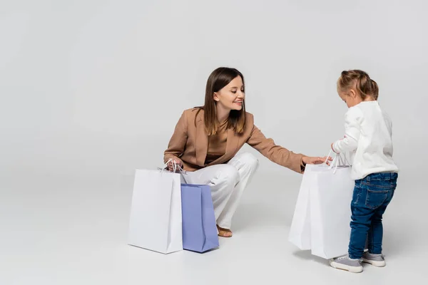 Happy and stylish mother holding shopping bags near girl with down syndrome on grey — Photo de stock