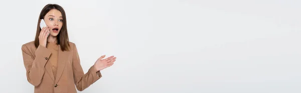 Mujer impactada en blazer gesto mientras hablaba en el teléfono celular aislado en gris, pancarta - foto de stock