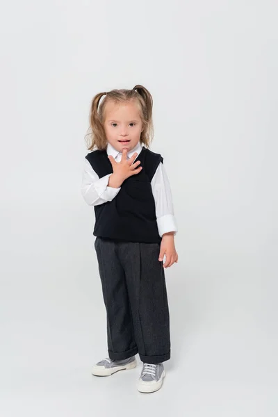 Повна довжина дитини з синдромом Дауна в жилеті і білій сорочці, що стоїть на сірій — стокове фото