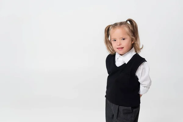 Happy kid with down syndrome in vest and white shirt standing isolated on grey — Stock Photo