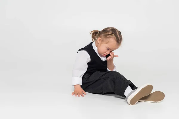 Full length of kid with down syndrome in vest and white shirt rubbing eye on grey — Photo de stock