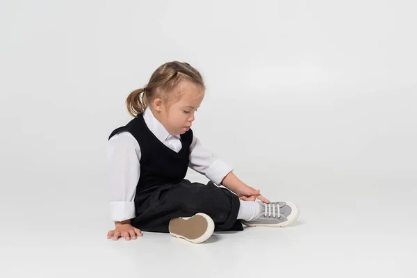 Full length of kid with down syndrome in vest and white shirt sitting on grey — Stockfoto