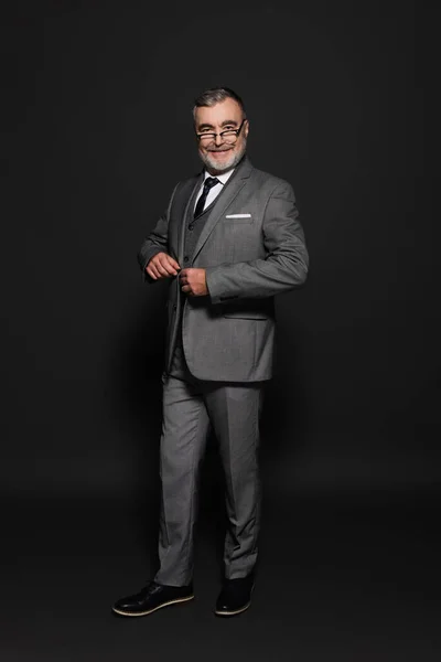 Full length view of happy senior man in suit looking at camera on dark grey — Stock Photo