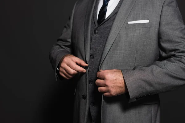 Cropped view of businessman buttoning blazer on dark grey background — стоковое фото