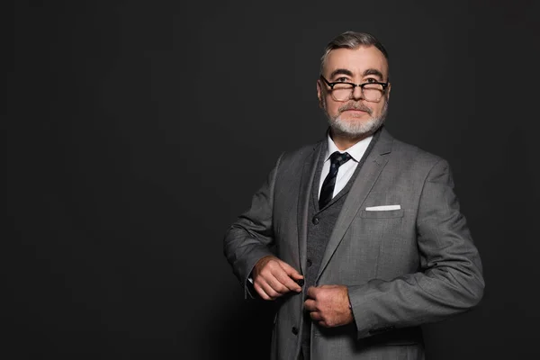 Grey-haired senior man in stylish suit looking at camera on dark grey — Photo de stock