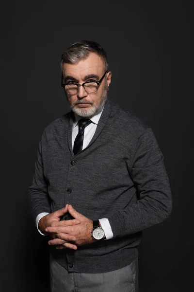 Serious businessman in jumper, tie and eyeglasses looking at camera on dark grey — Foto stock