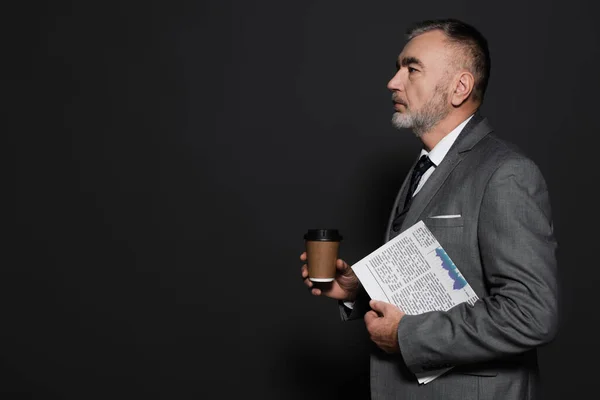 Side view of man in formal wear holding paper cup and newspaper on dark grey — Stock Photo