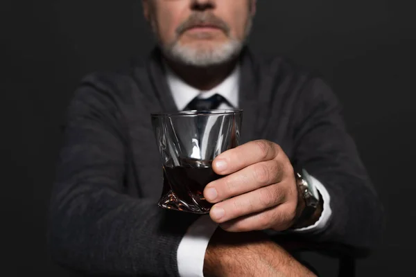 Cropped view of blurred man in grey jumper holding glass of whiskey isolated on black — Stock Photo