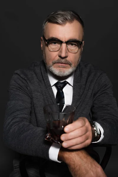 Stylish and serious senior man with glass of whiskey looking at camera on dark grey — Photo de stock