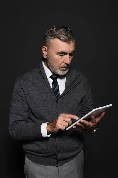 Grey-haired man in stylish clothes using digital tablet on dark grey — Stock Photo