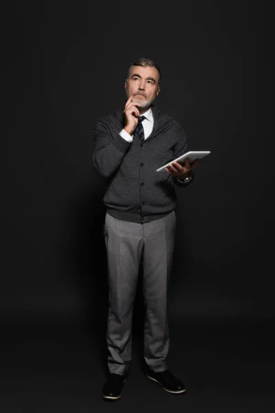 Full length view of pensive senior man with digital tablet looking away on dark grey - foto de stock