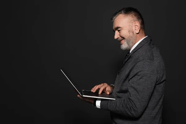 Side view of bearded senior man using digital tablet isolated on dark grey — стоковое фото