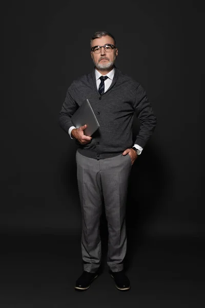 Full length view of senior stylish man standing with hand in pocket and laptop on dark grey — Fotografia de Stock