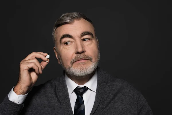 Senior bearded man in tie holding earphone isolated on dark grey — Fotografia de Stock