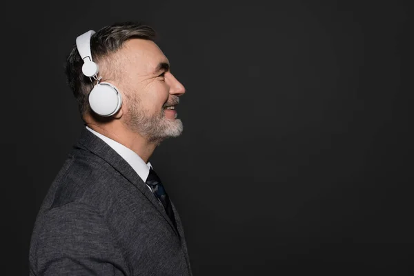 Side view of cheerful bearded man listening music in headphones isolated on black - foto de stock