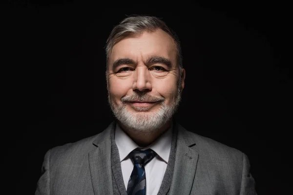 Cheerful bearded man in blazer and tie looking at camera isolated on black — Foto stock