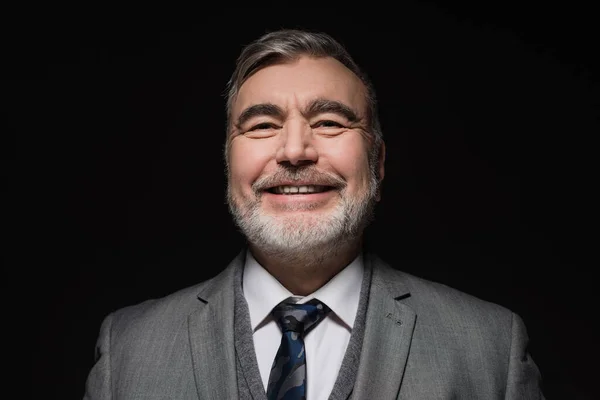 Cheerful bearded man in formal wear smiling at camera isolated on black — Foto stock