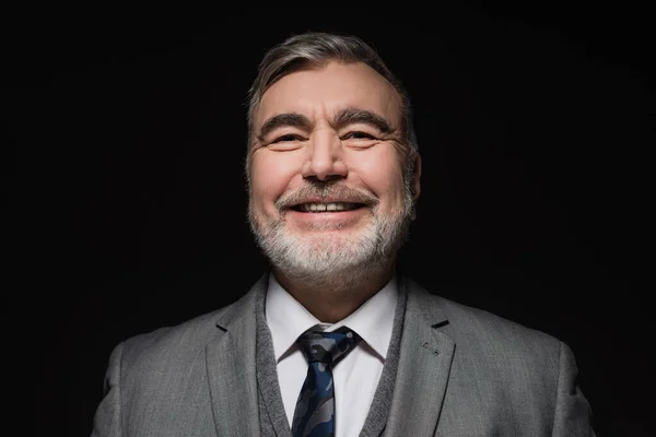 Cheerful bearded man in formal wear smiling at camera isolated on black — Stock Photo