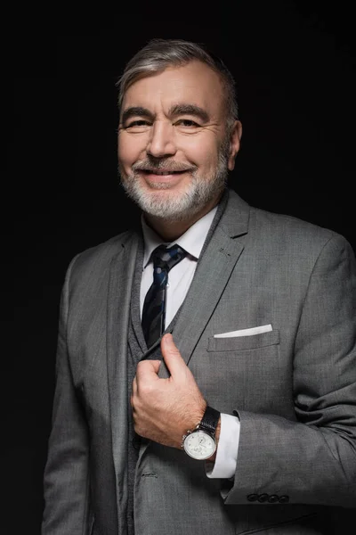 Joyful bearded man in grey blazer looking at camera isolated on black — Stockfoto