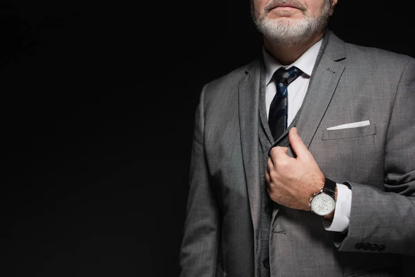 Cropped view of senior businessman in suit and tie isolated on black - foto de stock