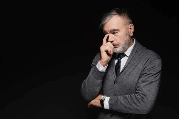 Pensive senior man in grey jumper touching face while thinking isolated on black - foto de stock