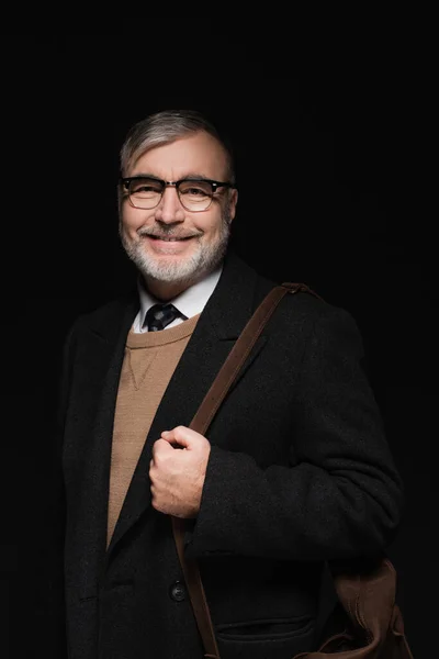 Happy senior man in trendy coat and eyeglasses looking at camera isolated on black — Stock Photo