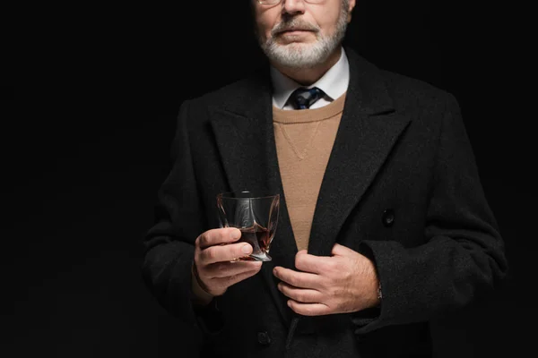 Partial view of senior man in stylish coat holding glass of whiskey isolated on black — Foto stock