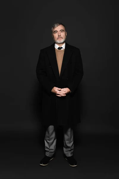 Full length view of grey-haired man in stylish coat looking at camera on grey — Photo de stock