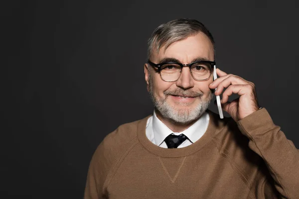 Smiling man in beige jumper and eyeglasses talking on cellphone isolated on grey — Stock Photo