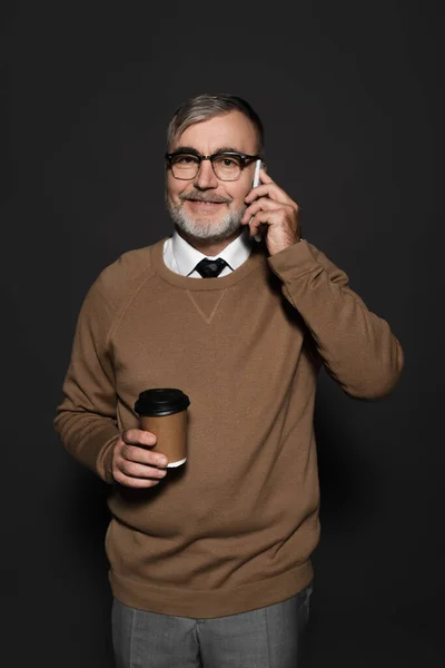 Happy senior man with takeaway drink talking on mobile phone on dark grey — Stock Photo