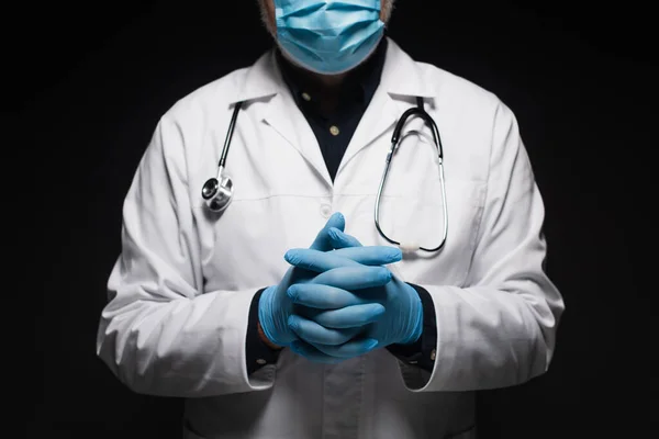 Обрізаний вид лікаря в медичній масці і латексних рукавичках, що стоять з загорнутими руками ізольовані на чорному — стокове фото