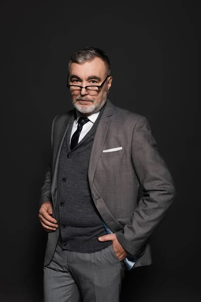 Senior businessman in suit standing with hand in pocket on dark grey — Fotografia de Stock