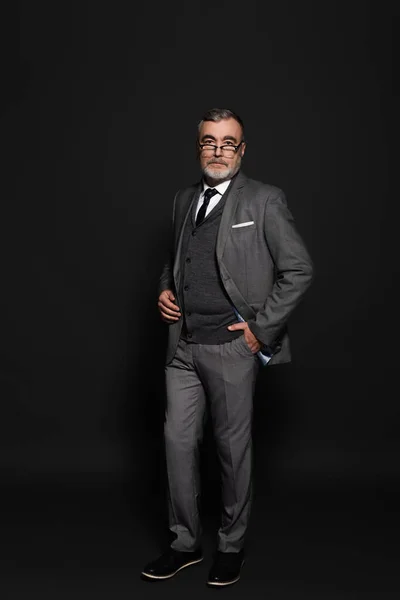 Full length view of senior businessman in stylish suit standing with hand in pocket on dark grey — Fotografia de Stock