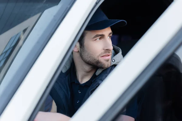 Courier in cap and uniform looking away in car — Stock Photo