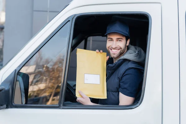 Smiling courier holding parcel and looking at camera in car — стоковое фото