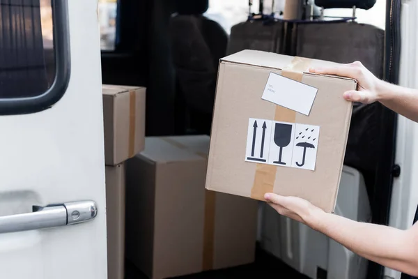 Cropped view of courier holding carton box with signs near car outdoors — Fotografia de Stock