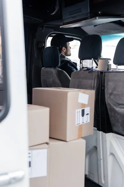 Young delivery man sitting near carton boxes in car — Foto stock