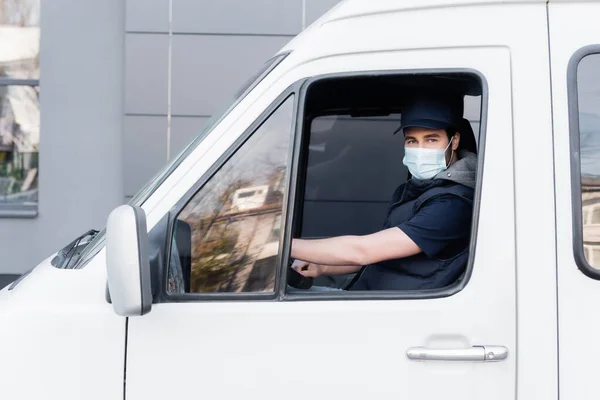 Courier in protective mask looking at camera while sitting in car — Stock Photo