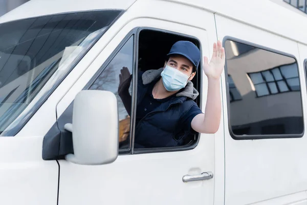 Courier in medical mask waving hand while driving auto — стокове фото