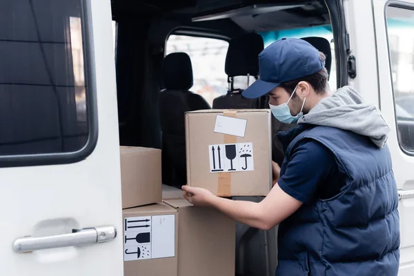 Courier in medical mask taking box from auto outdoors — Photo de stock