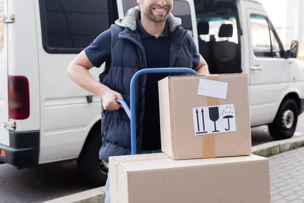 Cropped view of delivery man holding cart with cardboard boxes on urban street — Fotografia de Stock