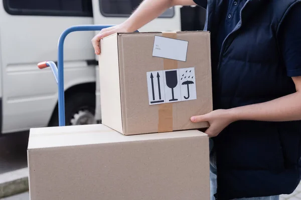 Cropped view of courier taking carton box from cart outdoors — стоковое фото