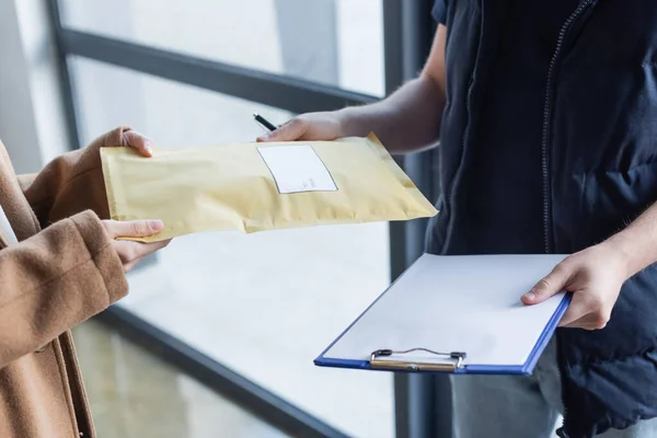 Cropped view of courier holding clipboard and giving parcel to woman in hallway — Foto stock