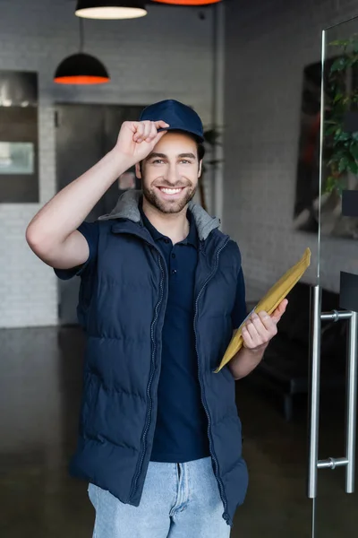 Smiling courier with parcel looking at camera in hallway — стоковое фото