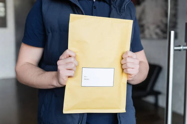 Cropped view of parcel with sticker in hands of blurred courier in hallway — стоковое фото
